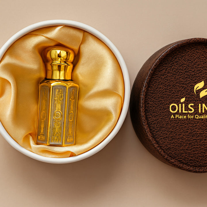 Gold perfume bottle in a white box with gold interior, next to a brown leather cover with 'Oils India In' branding.