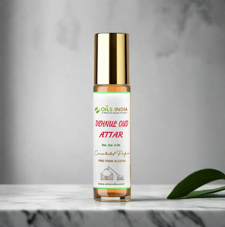 Roll-on bottle of Oils India Dehnila Oud Attar on a marble surface with a blurred plant and wall in the background.