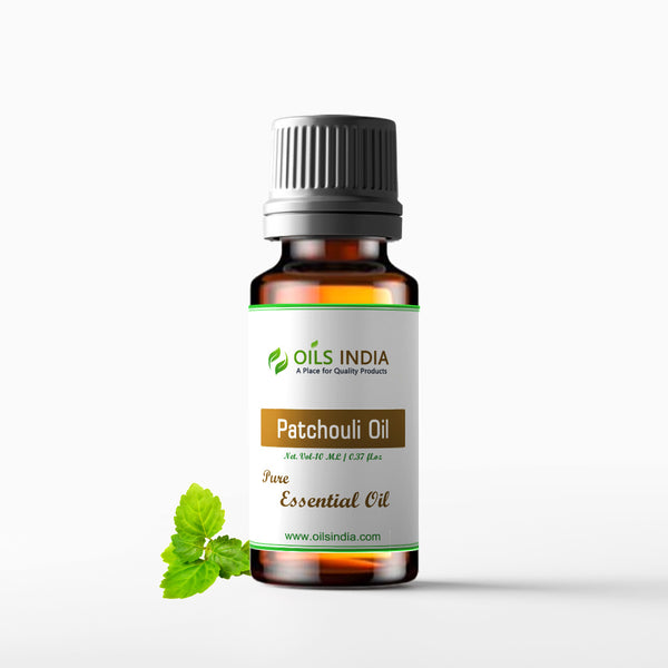 A bottle of Patchouli Essential Oil with a black cap and a label that reads 'Patchouli Oil - Pure Essential Oil'. The bottle is manufactured by Oils India and it is displayed against a white background with a sprig of mint leaves next to it.