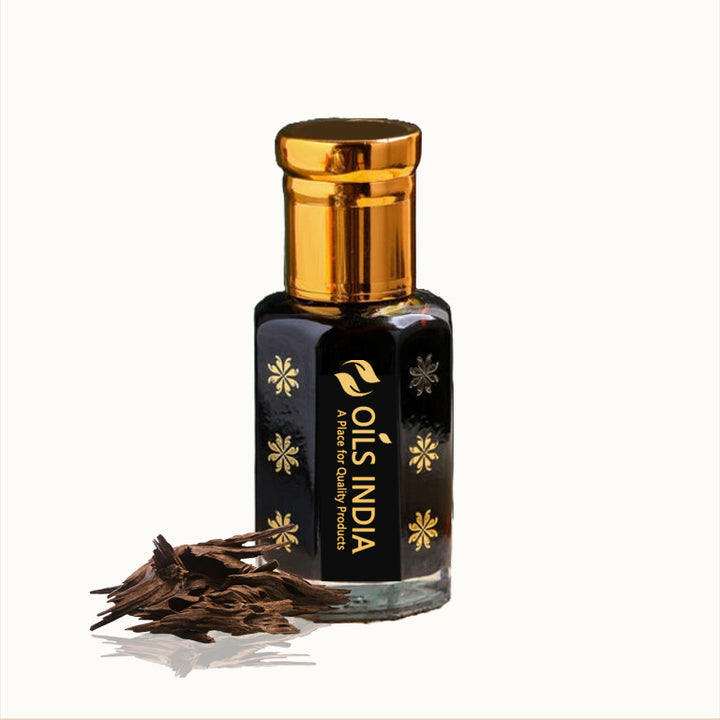 A dark glass bottle with a gold cap labeled 'Agarwood India' containing dark brown liquid, alongside Agarwood wood chips.